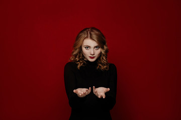 young cheerful red-haired girl in black clothes posing in the studio isolated on red background....