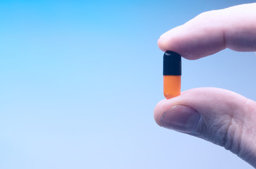 black and orange capsule in the hand of a man on a blue background