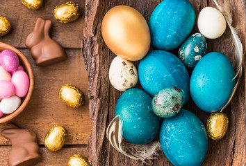 Easter blue and gold eggs, chocolate bunnies on wooden background.