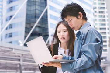 attractive business man and business woman holding computer laptop for discuss in business project at outdoor in modern city center.