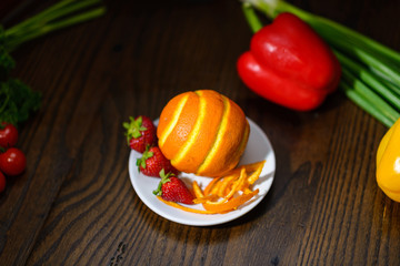 Orange with patterns and strawberries on a table with vegetables