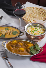 Indian curry food spread on a fancy dinner table with rice, laccha paratha, lamb aam wala, saffron malai kofta, red wine