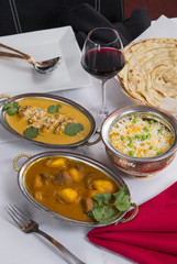 Indian curry food spread on a fancy dinner table with rice, laccha paratha, lamb aam wala, saffron malai kofta, red wine