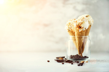 Caramel sauce ice cream in waffle cone with coffee beans on grey stone background. Summer food concept, copy space. Healthy gluten free ice-cream. Banner