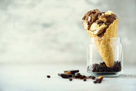 Chocolate and coffee ice cream in waffle cone with coffee beans on grey stone background. Summer food concept, copy space. Healthy gluten free ice-cream