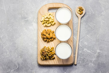 Nut mix and nut milk in glasses on wooden board on concrete background.  Top view, space for text.