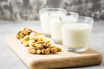 Nut mix, almonds, cashew, walnuts and nut milk in glasses on wooden board on concrete background. Selective focus, copy space. 