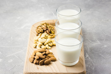 Almonds, cashew, walnuts and nut milk in glasses on wooden board on concrete background. Selective focus, copy space, closeup. 