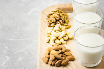 Almonds, cashew, walnuts and nut milk in glasses on wooden board on concrete background. Selective focus, copy space. 