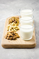 Almonds, cashew, walnuts and homemade nut milk in glasses on wooden board on concrete background. Selective focus, copy space. 