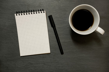 Blank gridded noted pad and cup of coffee - from above on dark slate table top background, with copy space