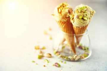 Green ice cream in waffle cone with chocolate and pistachio nuts on grey stone background. Summer food concept, copy space. Healthy gluten free ice-cream. Banner