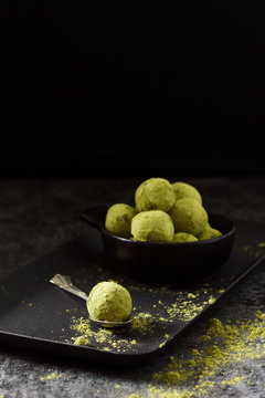 Pralinki zielone matcha z daktylami na ciemnym betonowym tle i czarnym talerzu