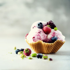 Pink ice cream with berries, strawberries, blueberries, raspberries, pistachios in waffle basket. Summer food concept, copy space. Healthy gluten free fruit ice-cream. Banner