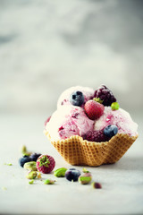 Pink ice cream with berries, strawberries, blueberries, raspberries, pistachios in waffle basket. Summer food concept, copy space. Healthy gluten free fruit ice-cream. Banner