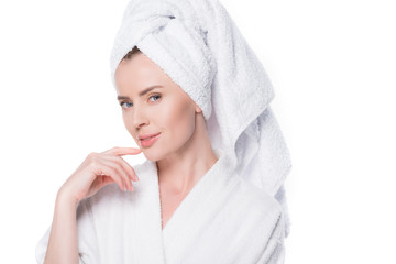 Obraz na płótnie Canvas Female with clean skin wearing bathrobe and towel on hair holding finger on chin isolated on white