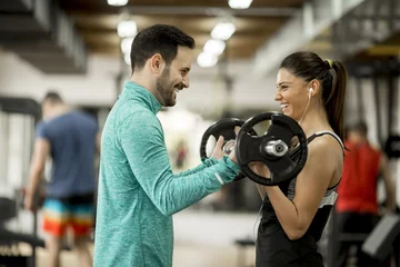 Tuinposter Young woman with personal trainer in gym © BGStock72