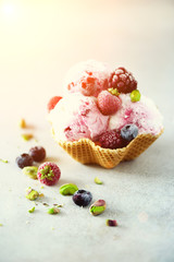 Pink ice cream with berries, strawberries, blueberries, raspberries, pistachios in waffle basket. Summer food concept, copy space. Healthy gluten free fruit ice-cream. Banner