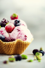 Pink ice cream with berries, strawberries, blueberries, raspberries, pistachios in waffle basket. Summer food concept, copy space. Healthy gluten free fruit ice-cream. Banner
