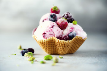 Pink ice cream with berries, strawberries, blueberries, raspberries, pistachios in waffle basket. Summer food concept, copy space. Healthy gluten free fruit ice-cream. Banner