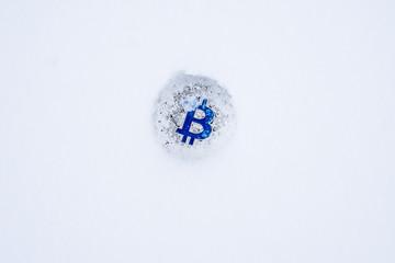 Coin of Bitcoin crypto currency thrown into the snow. Silver bitcoin with blue B in the snow alone.