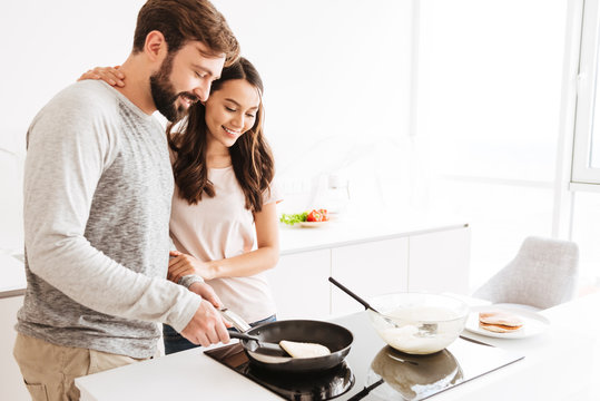 Portrait of a joyful young couple cooking pancakes