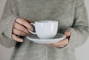 Young woman holding a white cup and saucer in his hands, drinking hot coffee. Space for your logo...