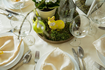 Beautiful served round table with decorations in dining room. Little yellow bunny, willow branches decorated with colorful Easter eggs. Spring holiday setting. Close-up