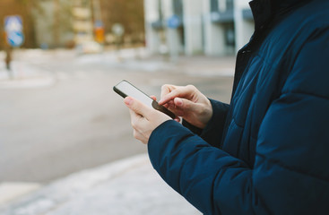 Mans hands typing text message on smart phone. Cropped image of young man stay on the street and using mobile phone.