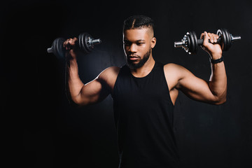 Fototapeta na wymiar handsome muscular african american man exercising with dumbbells on black
