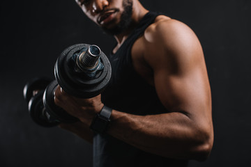 Fototapeta na wymiar cropped shot of muscular african american sportsman exercising with dumbbells on black