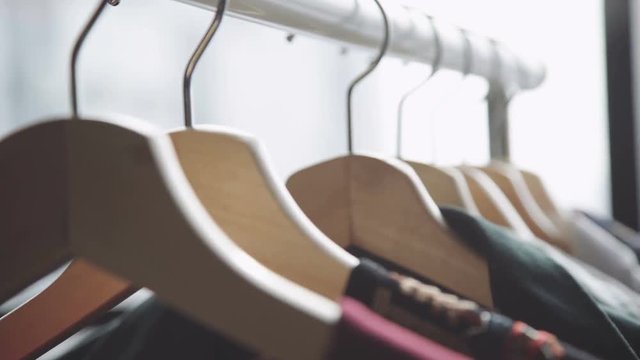 Close-up of female hands plucked a hanger with clothes. Woman's hands run across a rack of clothes. Dolly shot from the side. Woman's hand smoothing a colorful clothes. Close-up: a hanger for clothing
