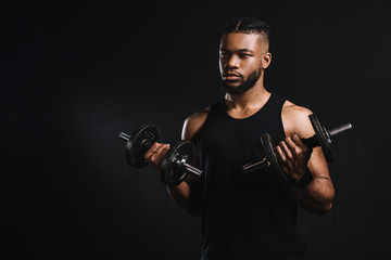 Fototapeta na wymiar young african american sportsman exercising with dumbbells and looking away isolated on black