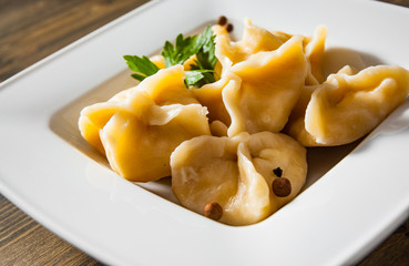 Meat dumplings - russian pelmeni, ravioli with meat on plate on a wooden background