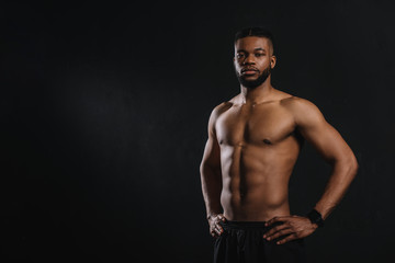 Fototapeta na wymiar muscular shirtless african american man standing with hands on waist and looking at camera isolated on black