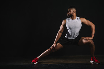 athletic young african american man in sportswear exercising and looking away on black