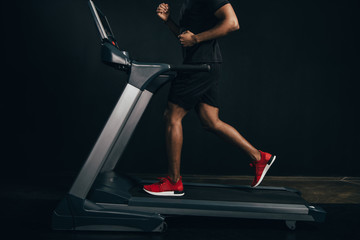 cropped shot of african american sportsman running on treadmill on black