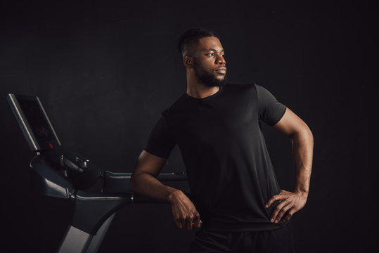 Athletic Young African American Man Leaning At Treadmill And Looking Away Isolated On Black