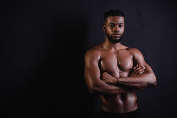 Fototapeta premium handsome muscular african american man standing with crossed arms and looking at camera on black