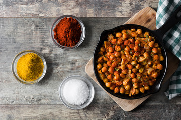 Fried spicy chickpeas in frying pan on wooden table. Top view