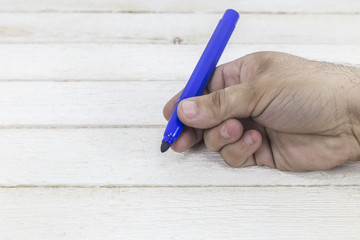 Hand holding a marker on white wooden background