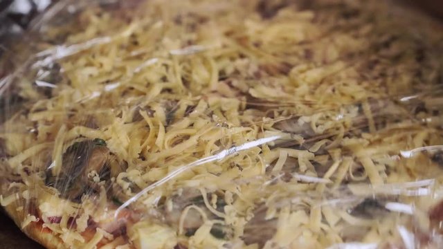 Woman packing pizza with cheese and mushrooms in food wrap for preservation