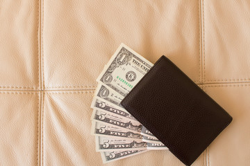 Brown leather wallet with dollars on the background of leather sofa