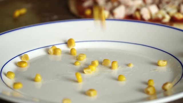 Canned corn grains fall into plate in slow motion