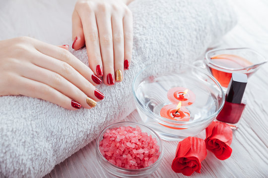 Red and golden manicure with spa essentials on white wooden table.