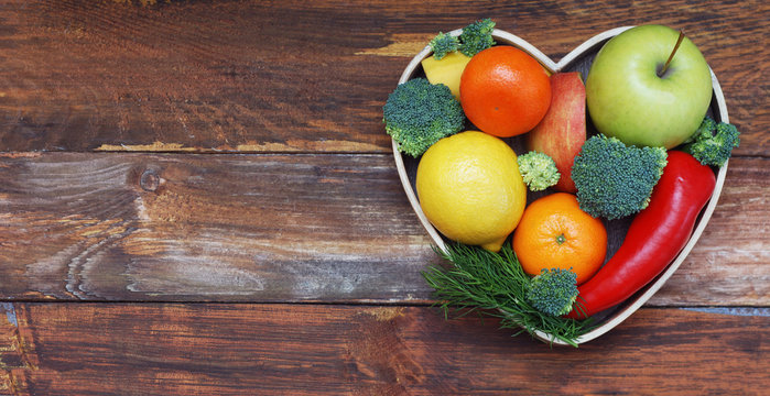 Fruits and Vegetables in Heart shaped Wooden Box. Broccoli, apples, Pepper, tangerine over Wooden Background. Banner. Health food Concept with copy space. - Powered by Adobe