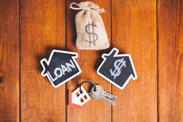 Two small houses over brown wood with a keyring and money sack