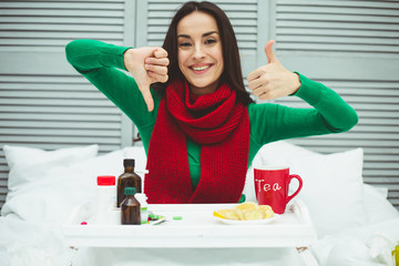 It is better to be treated without pills. A young smiling woman in a red scarf at home on the bed shows that tea and fruits with vitamins are better for treatment than tablets.