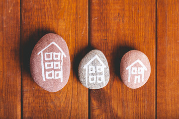 Three houses drawn on stones over brown wood.