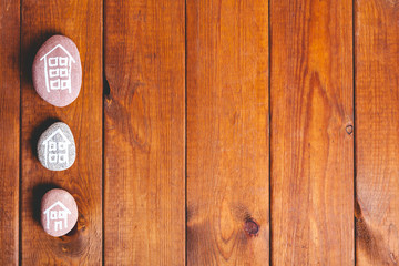 Fototapeta premium Three houses drawn on stones over brown wood.